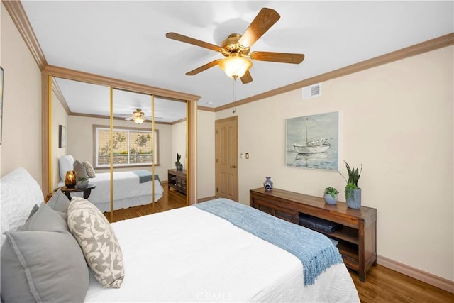 bedroom with a closet, visible vents, ornamental molding, wood finished floors, and baseboards