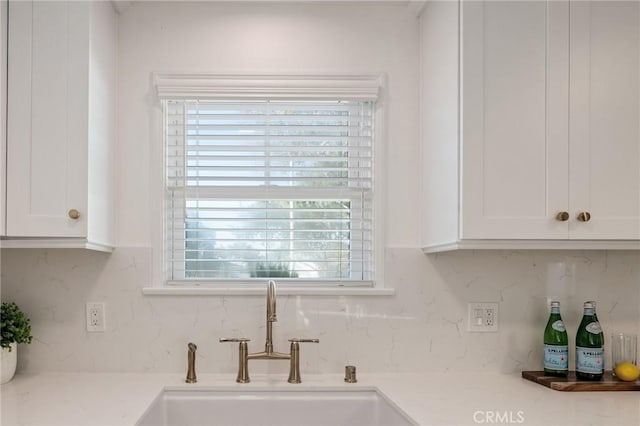 kitchen featuring light countertops, white cabinets, a sink, and backsplash