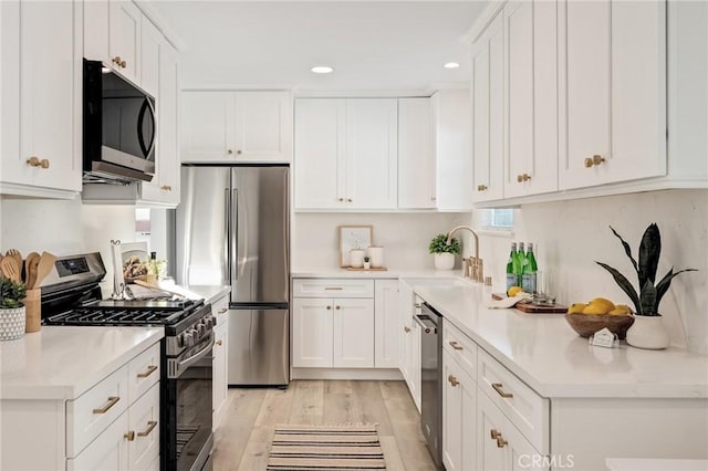 kitchen featuring light wood finished floors, stainless steel appliances, light countertops, white cabinetry, and a sink