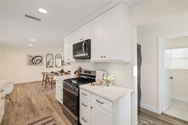 kitchen with stainless steel appliances, light countertops, visible vents, white cabinets, and light wood-type flooring