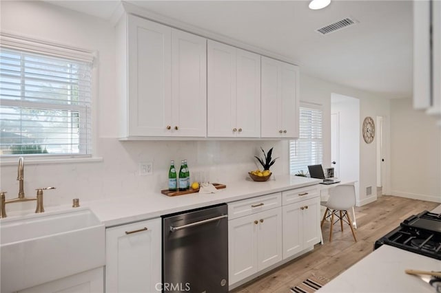 kitchen with light countertops, visible vents, stainless steel dishwasher, white cabinets, and a sink