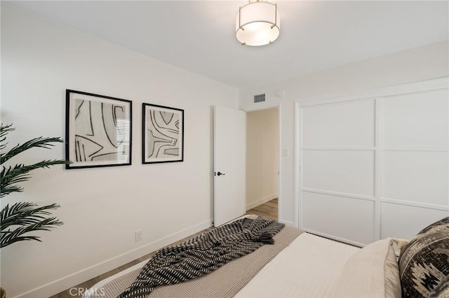 bedroom featuring a closet, wood finished floors, visible vents, and baseboards