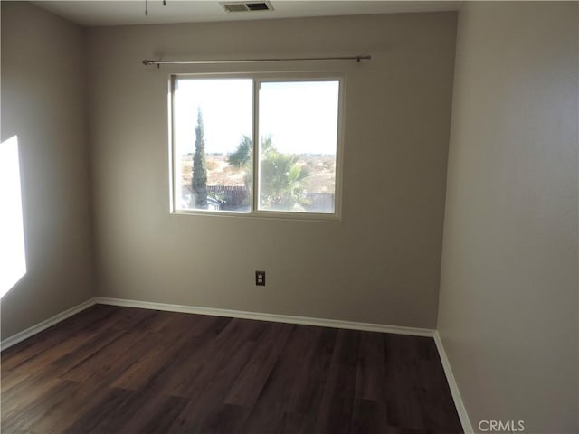 spare room featuring dark wood-style floors, visible vents, and baseboards