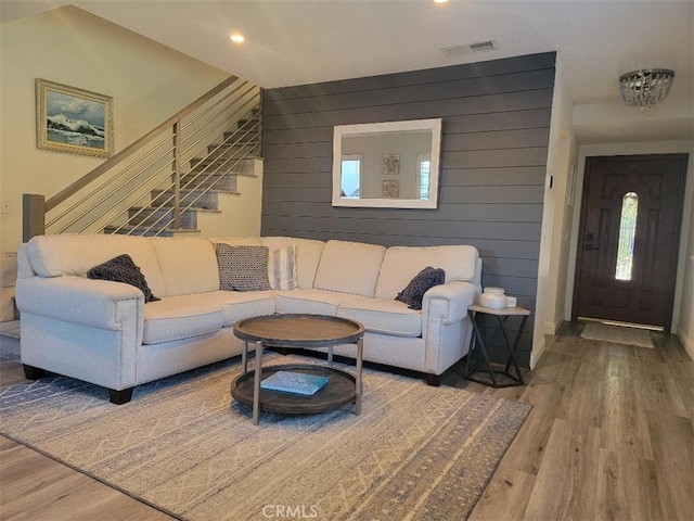 living area featuring a wealth of natural light, visible vents, stairway, wooden walls, and wood finished floors