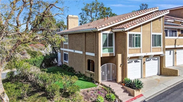 view of front of house featuring a garage, a tile roof, driveway, stucco siding, and a chimney