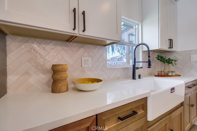 kitchen featuring white cabinets, light countertops, a sink, and backsplash