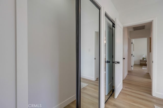 hall featuring light wood-style floors, baseboards, and visible vents