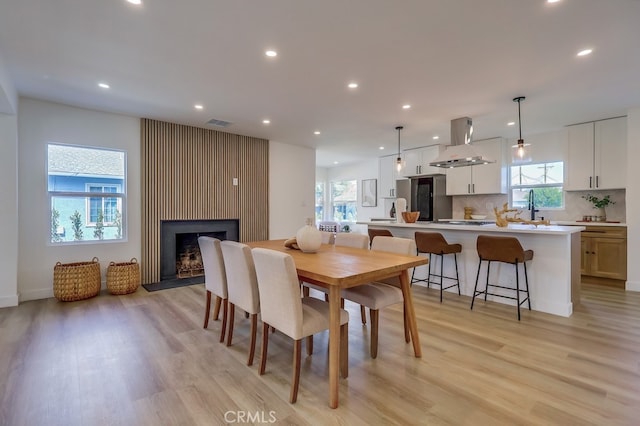 dining space with light wood-style floors, recessed lighting, a large fireplace, and visible vents