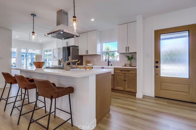 kitchen featuring white cabinets, island range hood, light countertops, and decorative light fixtures