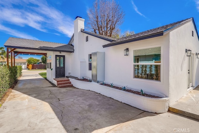 rear view of house with a chimney, a patio, and stucco siding