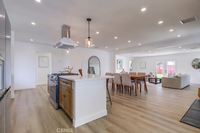 kitchen with decorative light fixtures, island exhaust hood, light countertops, open floor plan, and stainless steel gas range oven