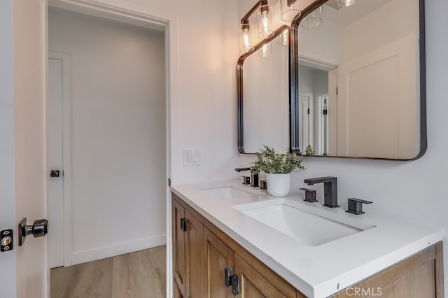 bathroom with double vanity, wood finished floors, a sink, and baseboards