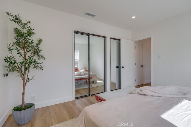 bedroom with light wood-style flooring, recessed lighting, visible vents, baseboards, and two closets