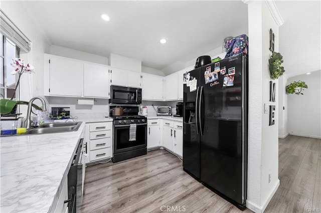 kitchen featuring light wood-style flooring, recessed lighting, a sink, white cabinets, and black appliances