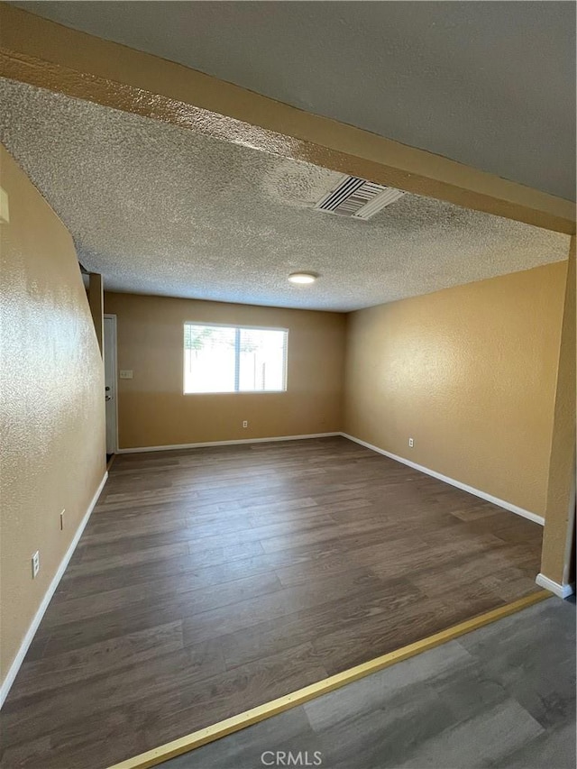 spare room with baseboards, a textured ceiling, visible vents, and dark wood-type flooring