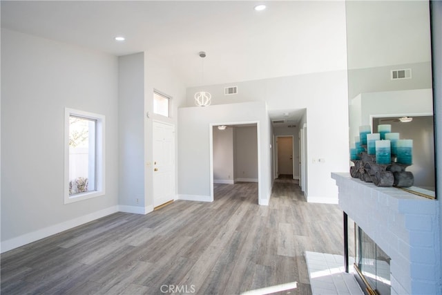 living area featuring high vaulted ceiling, wood finished floors, visible vents, and baseboards