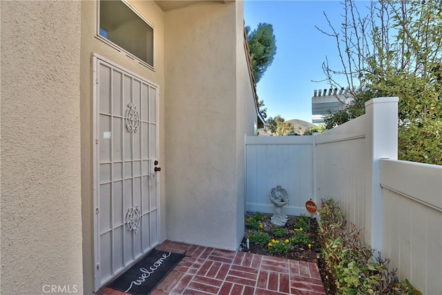 view of exterior entry with fence and stucco siding