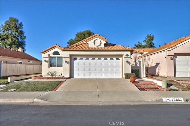 mediterranean / spanish house featuring concrete driveway, a tile roof, fence, and stucco siding