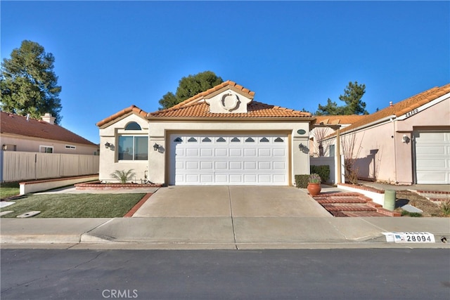 mediterranean / spanish-style house featuring concrete driveway, fence, a tiled roof, and stucco siding