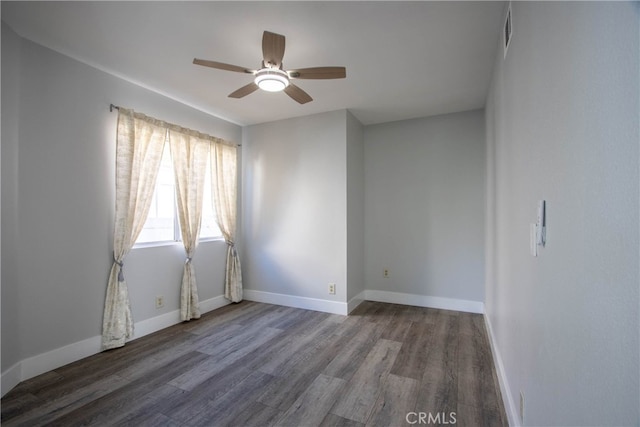 empty room featuring ceiling fan, visible vents, baseboards, and dark wood finished floors