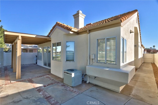 rear view of property featuring a tile roof, a patio, stucco siding, central AC unit, and fence