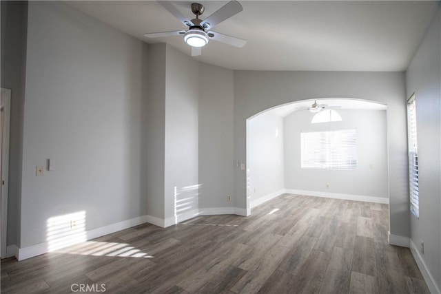 unfurnished room with dark wood-style floors, arched walkways, ceiling fan, and baseboards