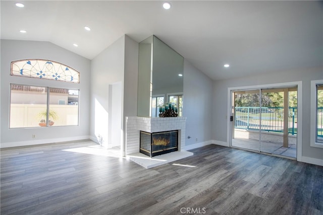 unfurnished living room featuring lofted ceiling, a brick fireplace, wood finished floors, and baseboards