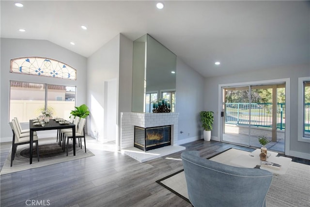 living area with baseboards, wood finished floors, vaulted ceiling, a brick fireplace, and recessed lighting