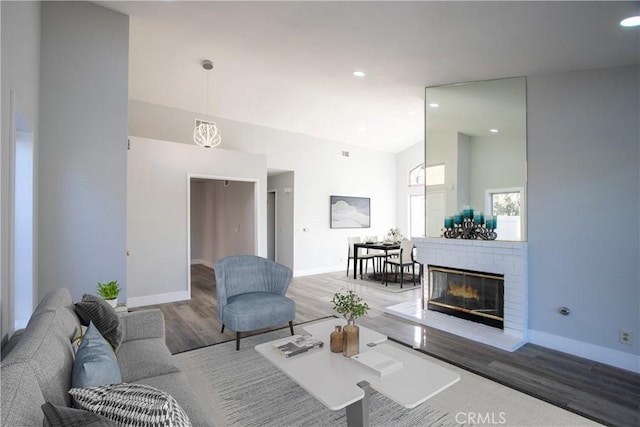 living area with light wood-style floors, a fireplace, high vaulted ceiling, and baseboards