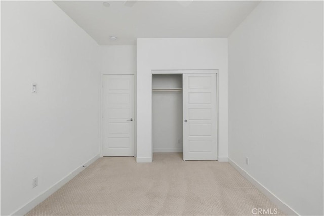 unfurnished bedroom featuring a closet, light colored carpet, and baseboards