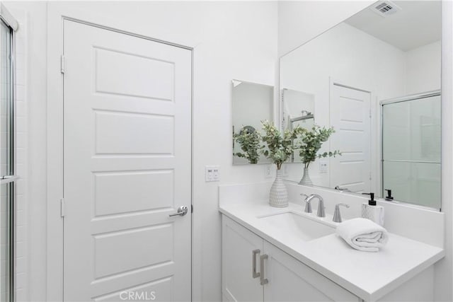 bathroom with a shower with shower door, visible vents, and vanity