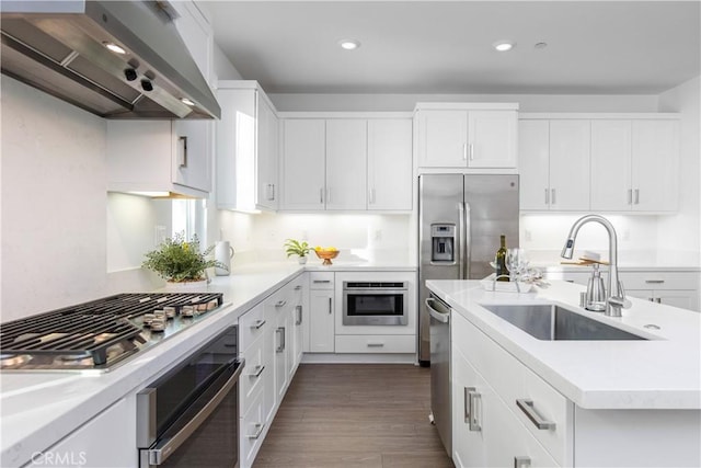 kitchen with light countertops, wall chimney range hood, a sink, and appliances with stainless steel finishes