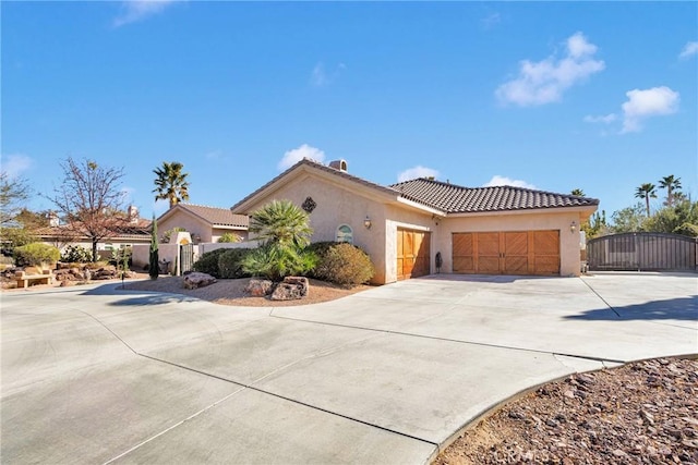 mediterranean / spanish house with a garage, a tile roof, concrete driveway, a gate, and stucco siding