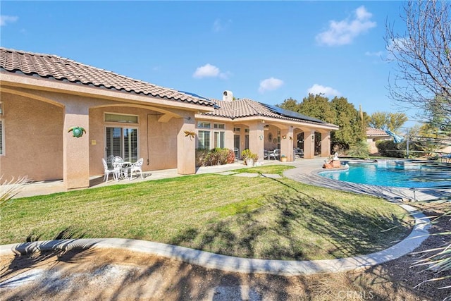 rear view of house featuring an outdoor pool, stucco siding, a yard, and solar panels