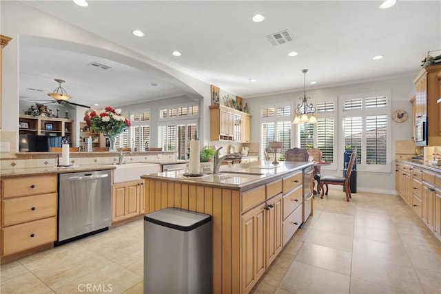 kitchen featuring a peninsula, a sink, light countertops, appliances with stainless steel finishes, and an island with sink