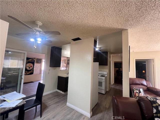 kitchen featuring white gas range, light countertops, visible vents, light wood-style floors, and dark cabinetry