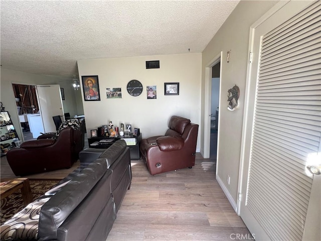 living area with light wood-type flooring, baseboards, visible vents, and a textured ceiling