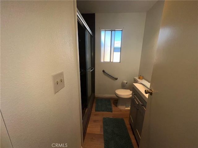 bathroom with toilet, a stall shower, wood finished floors, and vanity