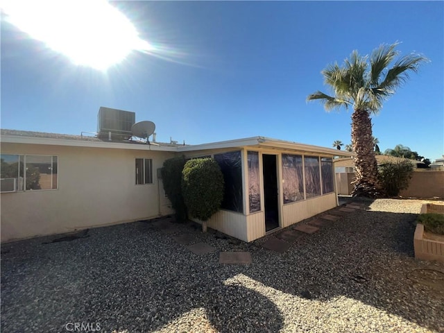 view of side of home with a sunroom, stucco siding, fence, and central AC unit