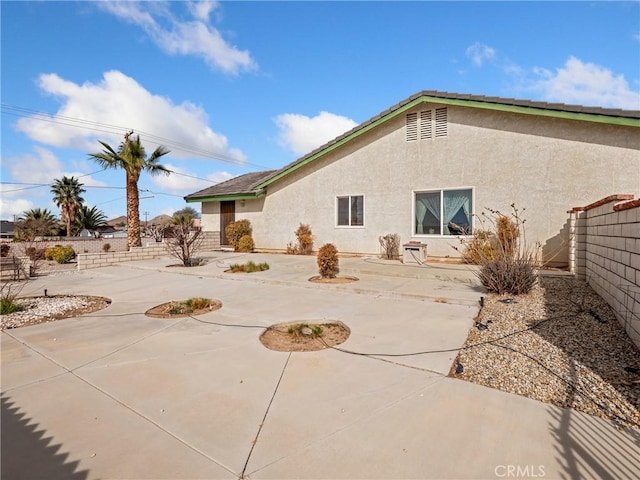 rear view of property with a patio area, fence, and stucco siding