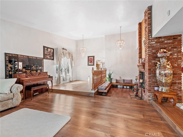 living room featuring a brick fireplace, wood finished floors, and an inviting chandelier