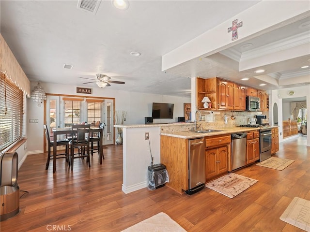 kitchen with a peninsula, stainless steel appliances, a sink, light countertops, and brown cabinetry