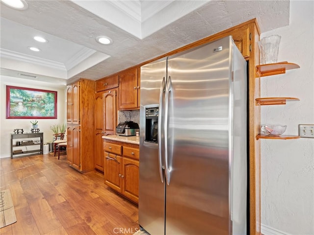 kitchen featuring a raised ceiling, light wood-style flooring, ornamental molding, light countertops, and stainless steel refrigerator with ice dispenser