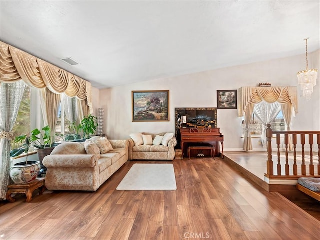 living room with plenty of natural light, wood finished floors, visible vents, and a notable chandelier