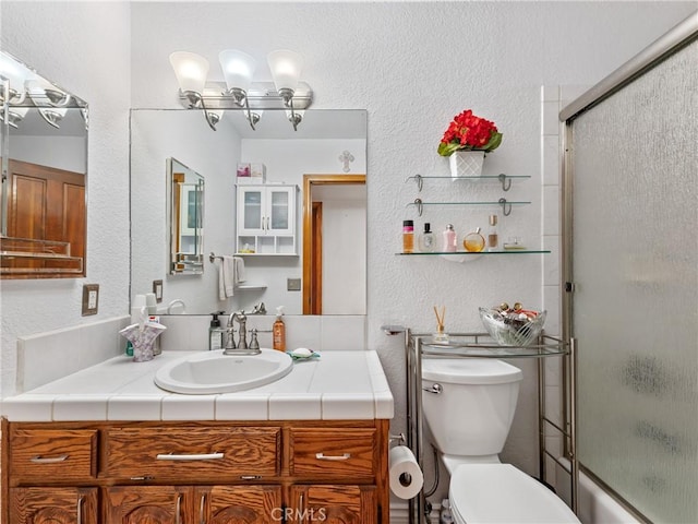 bathroom with toilet, a textured wall, bath / shower combo with glass door, and vanity