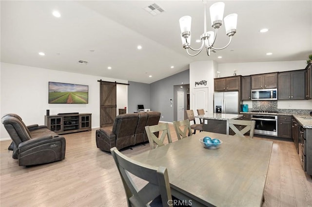 dining area with a notable chandelier, light wood finished floors, visible vents, a barn door, and vaulted ceiling