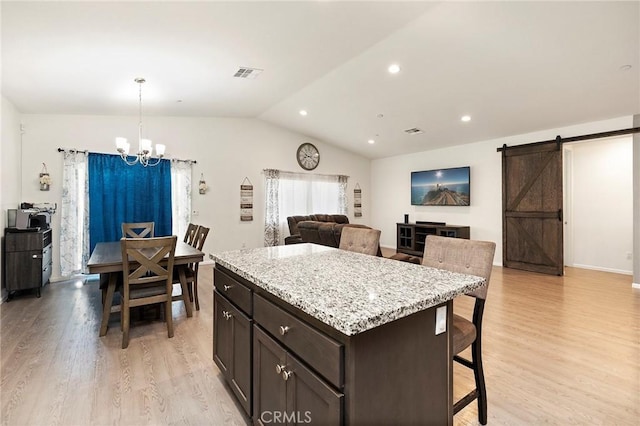 kitchen with a barn door, visible vents, lofted ceiling, light wood-style flooring, and pendant lighting