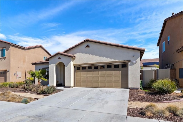 mediterranean / spanish-style house with concrete driveway, a tile roof, an attached garage, fence, and stucco siding