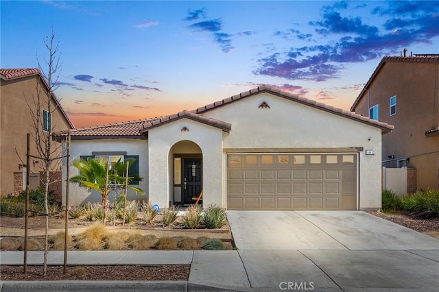 mediterranean / spanish-style home with an attached garage, driveway, a tile roof, and stucco siding