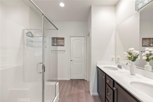 full bathroom with a stall shower, double vanity, a sink, and wood finished floors